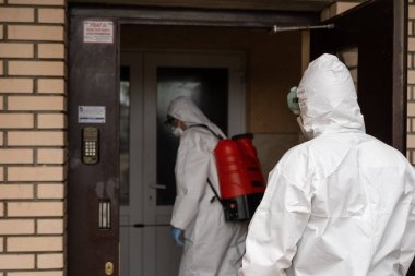 UKRAINE, KYIV - 20 Mayıs 2020: Beyaz koruyucu giysili ve maskeli iki adam bina içinde iç yüzeyleri dezenfekte ederken koronavirüs salgını enfeksiyonu önleme ve kontrol etme amaçlı