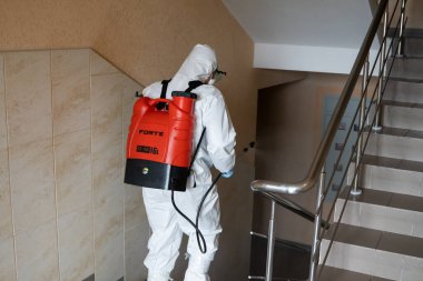 UKRAINE, KYIV - 20 Mayıs 2020: Beyaz koruyucu giysili ve maskeli adam salgının önlenmesi ve kontrol edilmesi için koronavirüs salgını sırasında iç yüzeyleri sterilize ediyor..