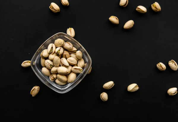 Pistazien in einem kleinen Teller mit verstreuten Mandelnüssen um einen Teller auf einer schwarzen Oberfläche. Pistazie ist eine gesunde vegetarische Proteinnahrung. Natürliche Nüsse Snacks. — Stockfoto