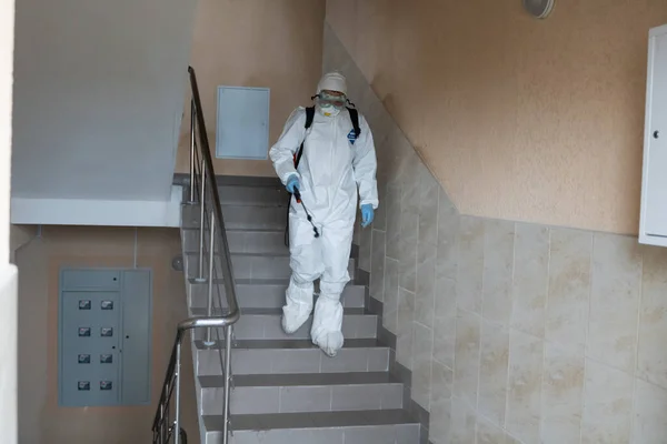 UKRAINE, KYIV - May 20, 2020: Man in a white protective suit and mask is disanitizing interior surfaces inside buildings while the coronavirus epidemic for infection prevention and control of epidemic . — стоковое фото