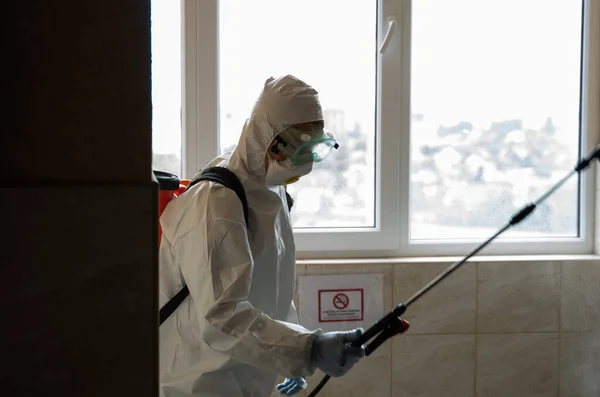 UKRAINE, KYIV - 20 mai 2020 : L'homme en costume et masque de protection blanc assainit les surfaces intérieures à l'intérieur des bâtiments tandis que l'épidémie de coronavirus pour la prévention des infections et la lutte contre l'épidémie. — Photo