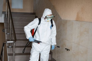 UKRAINE, KYIV - 20 Mayıs 2020: Beyaz koruyucu giysili ve maskeli adam salgının önlenmesi ve kontrol edilmesi için koronavirüs salgını sırasında iç yüzeyleri sterilize ediyor..