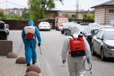UKRAINE, KYIV - 20 Mayıs 2020: Beyaz koruyucu giysili ve maskeli bir adam, koronavirüs salgını sırasında binanın iç yüzeylerini dezenfekte ettikten sonra sokakta yürüyor..