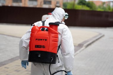 UKRAINE, KYIV - 20 Mayıs 2020: Beyaz koruyucu giysili ve maskeli bir adam, koronavirüs salgını sırasında binanın iç yüzeylerini dezenfekte ettikten sonra sokakta yürüyor..