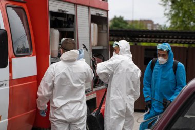 UKRAINE, KYIV - 20 Mayıs 2020: Beyaz koruyucu giysili ve maskeli bir adam bir arabanın yanında duruyor ve koronavirüs salgını sırasında iç yüzeyleri sterilize etmeye hazırlanıyor..