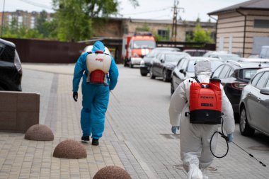 UKRAINE, KYIV - 20 Mayıs 2020: Beyaz koruyucu giysili ve maskeli bir adam, koronavirüs salgını sırasında binanın iç yüzeylerini dezenfekte ettikten sonra sokakta yürüyor..