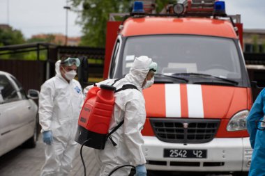 UKRAINE, KYIV - 20 Mayıs 2020: Beyaz koruyucu giysili ve maskeli bir adam bir arabanın yanında duruyor ve koronavirüs salgını sırasında iç yüzeyleri sterilize etmeye hazırlanıyor..