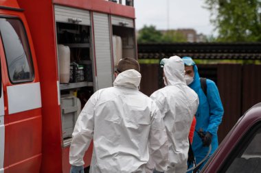 UKRAINE, KYIV - 20 Mayıs 2020: Beyaz koruyucu giysili ve maskeli bir adam bir arabanın yanında duruyor ve koronavirüs salgını sırasında iç yüzeyleri sterilize etmeye hazırlanıyor..