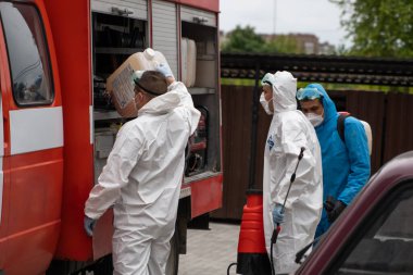 UKRAINE, KYIV - 20 Mayıs 2020: Beyaz koruyucu giysili ve maskeli bir adam bir arabanın yanında duruyor ve koronavirüs salgını sırasında iç yüzeyleri sterilize etmeye hazırlanıyor..