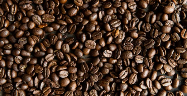 Roasted arabica coffee beans scattered on a wooden table. Fresh coffee beans. — Stock Photo, Image