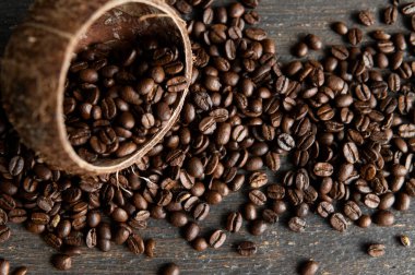 Kavrulmuş Arap kahve çekirdekleri bir hindistan cevizinden ahşap bir masaya saçılmış. Taze kahve çekirdekleri.