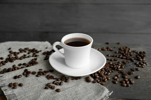 커피 잔에 볶은 커피 원두를 나무로 된 테이블 배경 위에 놓는다. 나무 탁자 위에는 커피 원두가 흩어져 있는 검은 커피 덩어리가 있었다. 신선 한 커피 콩. — 스톡 사진