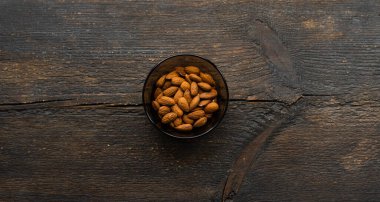 Bademler eski ahşap bir masada küçük bir tabakta. Badem sağlıklı bir vejetaryen protein yiyeceğidir. Doğal çerezler.