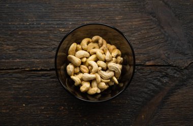 Arka plan olarak eski ahşap bir masada küçük bir tabakta kaju fıstığı. Kaju fıstığı sağlıklı bir vejetaryen protein yiyeceğidir..