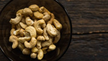Arka plan olarak eski ahşap bir masada küçük bir tabakta kaju fıstığı. Kaju fıstığı sağlıklı bir vejetaryen protein yiyeceğidir..