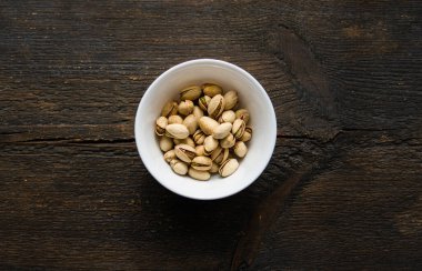 Eski ahşap bir masada küçük bir tabakta şam fıstığı. Pistachio sağlıklı bir vejetaryen protein yiyeceğidir. Doğal çerezler.