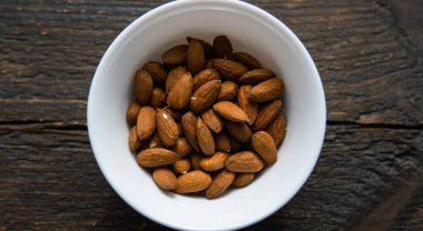Bademler eski ahşap bir masada küçük bir tabakta. Badem sağlıklı bir vejetaryen protein yiyeceğidir. Doğal çerezler.