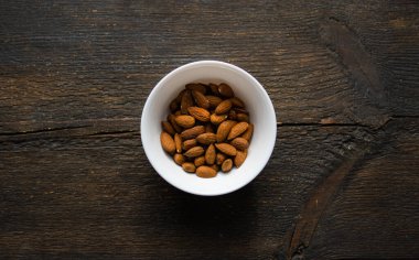 Bademler eski ahşap bir masada küçük bir tabakta. Badem sağlıklı bir vejetaryen protein yiyeceğidir. Doğal çerezler.