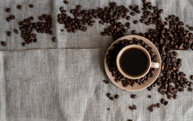 Keten arka planda kavrulmuş kahve çekirdekli kahve fincanı. Bir kupa sade kahve ve dağınık kahve çekirdeği. Taze kahve çekirdekleri.