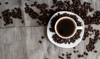 Keten arka planda kavrulmuş kahve çekirdekli kahve fincanı. Bir kupa sade kahve ve dağınık kahve çekirdeği. Taze kahve çekirdekleri.