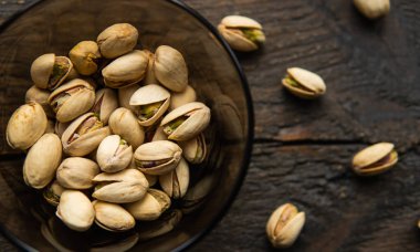 Arka plan olarak eski ahşap bir masada, bir tabağın etrafına saçılmış badem cevizleri olan küçük bir tabakta şam fıstığı. Pistachio sağlıklı bir vejetaryen protein yiyeceğidir. Doğal çerezler.