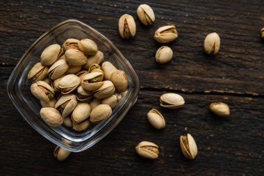 Arka plan olarak eski ahşap bir masada, bir tabağın etrafına saçılmış badem cevizleri olan küçük bir tabakta şam fıstığı. Pistachio sağlıklı bir vejetaryen protein yiyeceğidir. Doğal çerezler.