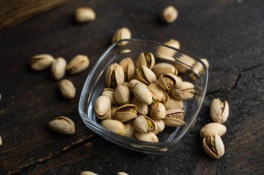 Arka plan olarak eski ahşap bir masada, bir tabağın etrafına saçılmış badem cevizleri olan küçük bir tabakta şam fıstığı. Pistachio sağlıklı bir vejetaryen protein yiyeceğidir. Doğal çerezler.