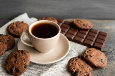Kurabiyeli kahve fincanı ve tahta masa arkasında çikolata. Bir fincan sade kahve ve çikolatalı kurabiye. Taze kahve çekirdekleri.