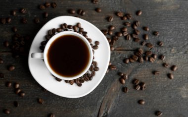 Ahşap masa arkasında kavrulmuş kahve çekirdekli kahve fincanı. Bir kupa sade kahve ve ahşap bir masanın üzerinde kahve çekirdekleri. Taze kahve çekirdekleri.