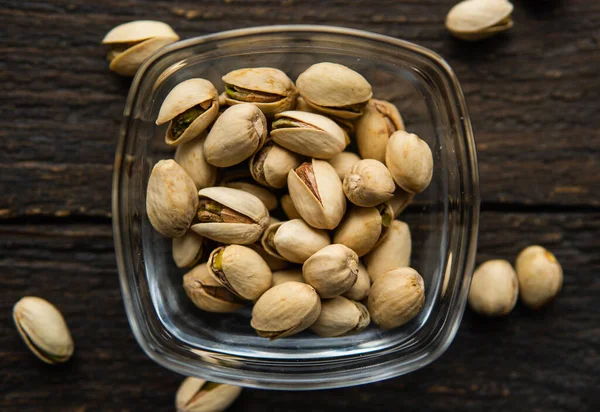 Pistachios in a small plate with scattered nuts of almonds around a plate on a vintage wooden table as a background. Pistachio is a healthy vegetarian protein nutritious food. Natural nuts snacks. — Stock Photo, Image