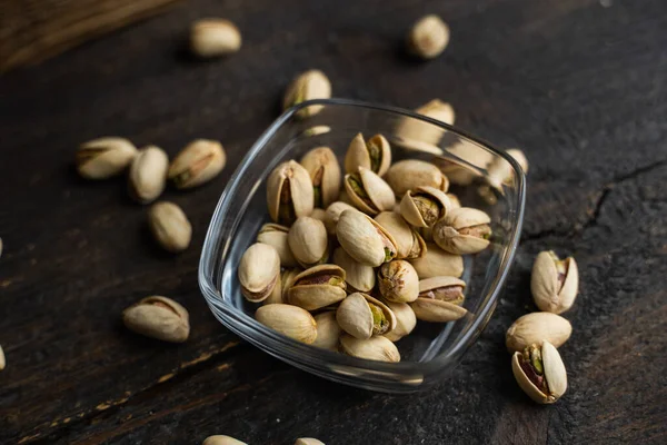 Pistachios in a small plate with scattered nuts of almonds around a plate on a vintage wooden table as a background. Pistachio is a healthy vegetarian protein nutritious food. Natural nuts snacks. — Stock Photo, Image