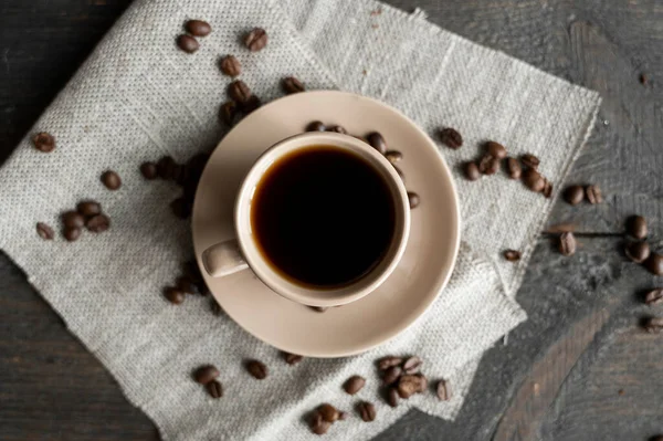 커피 잔에는 나무로 된 탁자 위에 커피 원두가 흩어져 있다. 아마포 직물 위에 있는 검은 커피 덩어리. — 스톡 사진