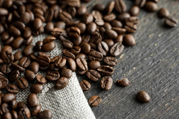 Grãos de café em um tecido de linho e em um fundo de mesa de madeira. Grãos de café arábica frescos. — Fotografia de Stock