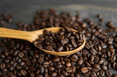 Taze kavrulmuş Arabika kahve çekirdekleri ahşap bir kaşıkta ve kahve çekirdekleri ahşap bir masanın üzerine serpilmiş..