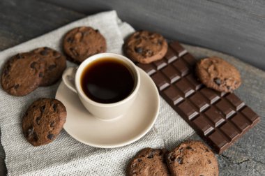 Kurabiyeli kahve fincanı ve tahta masa arkasında çikolata. Bir fincan sade kahve ve çikolatalı kurabiye. Taze kahve çekirdekleri.
