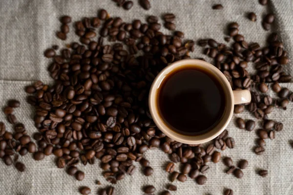 Кофейная чашка с жареными кофейными зернами на льняном фоне. Кружка черного кофе с разбросанными кофейными зёрнами. Свежий кофе в зернах. — стоковое фото