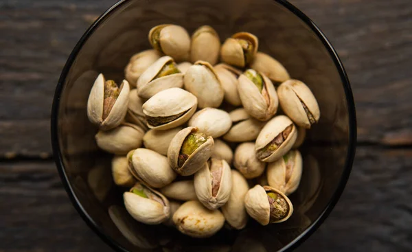 Pistachios in a small plate on a vintage wooden table. Pistachio is a healthy vegetarian protein nutritious food. Natural nuts snacks. — Stock Photo, Image