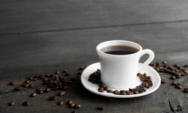 Ahşap masa arkasında kavrulmuş kahve çekirdekli kahve fincanı. Bir kupa sade kahve ve ahşap bir masanın üzerinde kahve çekirdekleri. Taze kahve çekirdekleri.