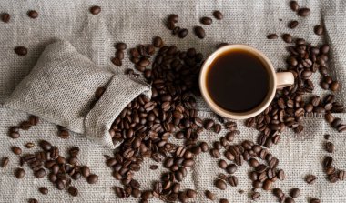 Keten poşetinden yayılmış kahve ve bir fincan koyu kahve Espresso ya da ahşap bir masanın üzerinde duran Americano. Keten tekstil üzerine taze Arap kahvesi. Aromatik taze demlenmiş kahve..