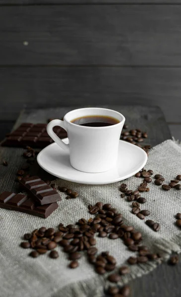 코 오피 컵 에 쿠키 와 초컬릿 을 넣고 커피 원두를 아마포와 나무 식탁 위에 펼쳐 놓는다. 검은 커피 덩어리. — 스톡 사진