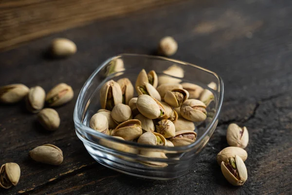 Pistachios in a small plate with scattered nuts of almonds around a plate on a vintage wooden table as a background. Pistachio is a healthy vegetarian protein nutritious food. Natural nuts snacks. — Stock Photo, Image