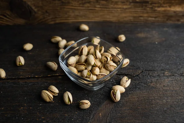 Pistachios in a small plate with scattered nuts of almonds around a plate on a vintage wooden table as a background. Pistachio is a healthy vegetarian protein nutritious food. Natural nuts snacks. — Stock Photo, Image