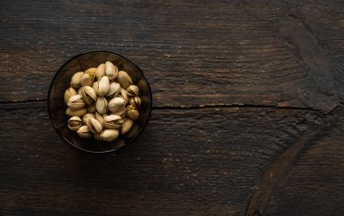 Eski ahşap bir masada küçük bir tabakta şam fıstığı. Pistachio sağlıklı bir vejetaryen protein yiyeceğidir. Doğal çerezler.