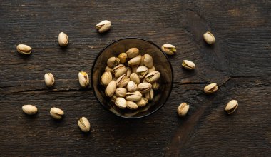 Arka plan olarak eski ahşap bir masada, bir tabağın etrafına saçılmış badem cevizleri olan küçük bir tabakta şam fıstığı. Pistachio sağlıklı bir vejetaryen protein yiyeceğidir. Doğal çerezler.