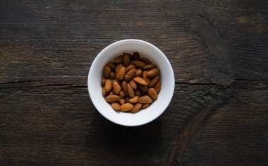 Bademler eski ahşap bir masada küçük bir tabakta. Badem sağlıklı bir vejetaryen protein yiyeceğidir. Doğal çerezler.