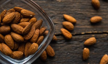 Bademler, arka plan olarak eski ahşap bir masada, tabağın etrafına saçılmış badem fındıkları olan küçük bir tabakta. Badem sağlıklı bir vejetaryen protein yiyeceğidir. Doğal çerezler.