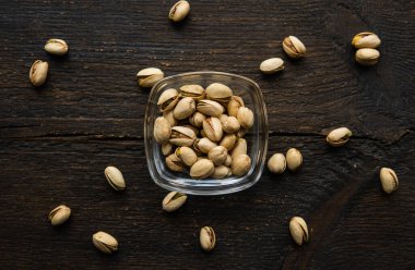 Arka plan olarak eski ahşap bir masada, bir tabağın etrafına saçılmış badem cevizleri olan küçük bir tabakta şam fıstığı. Pistachio sağlıklı bir vejetaryen protein yiyeceğidir. Doğal çerezler.