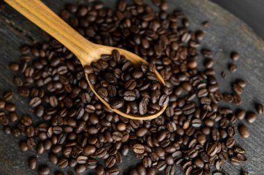 Taze kavrulmuş Arabika kahve çekirdekleri ahşap bir kaşıkta ve kahve çekirdekleri ahşap bir masanın üzerine serpilmiş..