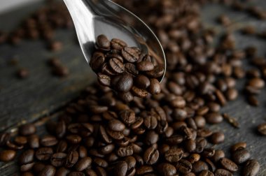 Taze kavrulmuş Arabika kahve çekirdekleri metal kaşıkta ve kahve çekirdekleri ahşap masada serpilmiş..