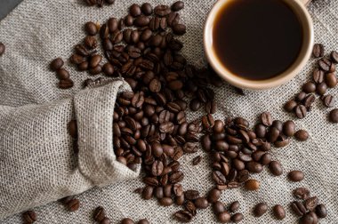 Keten poşetinden yayılmış kahve ve bir fincan koyu kahve Espresso ya da ahşap bir masanın üzerinde duran Americano. Keten tekstil üzerine taze Arap kahvesi. Aromatik taze demlenmiş kahve..